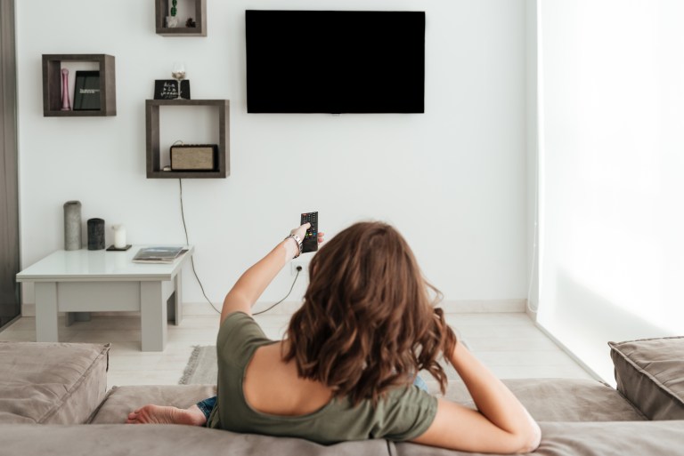 back view of casual woman sitting on sofa and watching tv in home